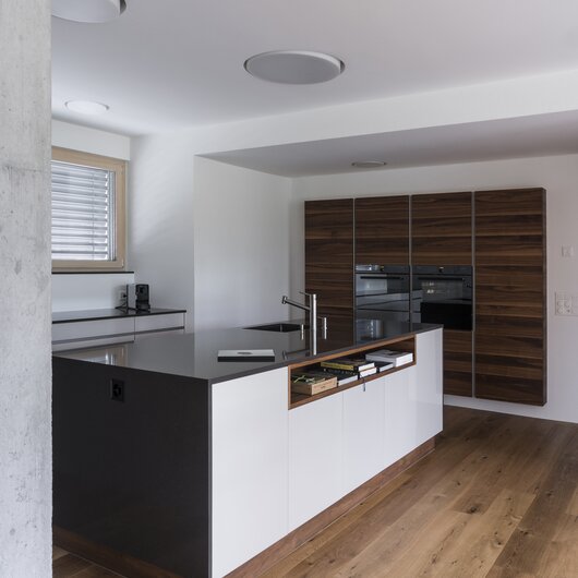 Referenz Hugentobler AG aus Branau, Wil - Moderne Küche mit dunkler Silestone Merope Oberfläche, in weiss mit warmen Holz.